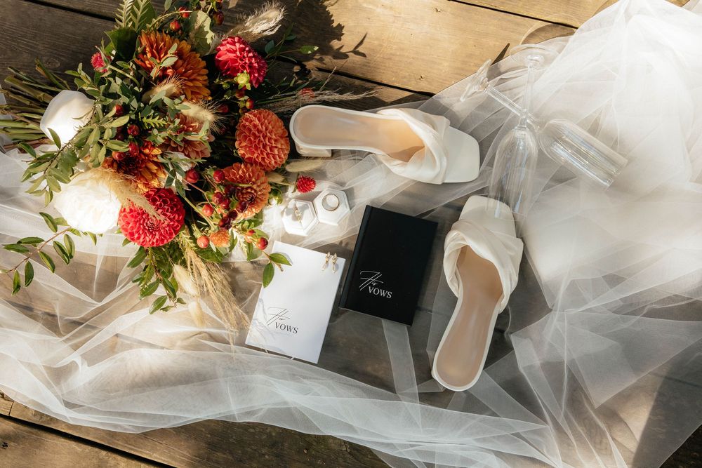 Elegant wedding vow books and delicate tulle fabric arranged with coral flowers and greenery on a rustic wooden surface.