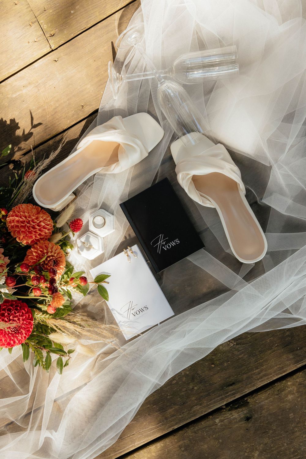 Wedding vow books and delicate white tulle veil arranged on rustic wooden surface with soft lighting.