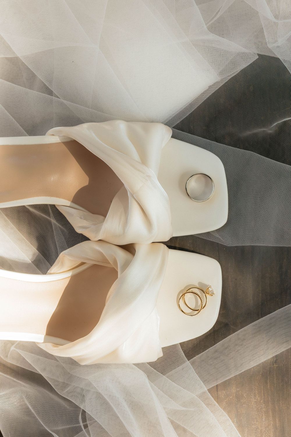 Delicate white tulle fabric with wedding rings creates an ethereal bridal still life composition.