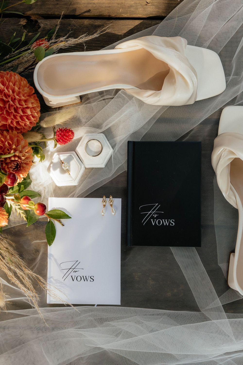 White wedding vow books displayed with flowing tulle fabric and floral decorations on a dark surface.