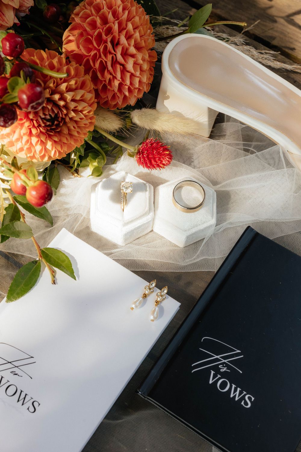 Navy blue vow books with coral dahlias and greenery arranged artistically on wooden surface.