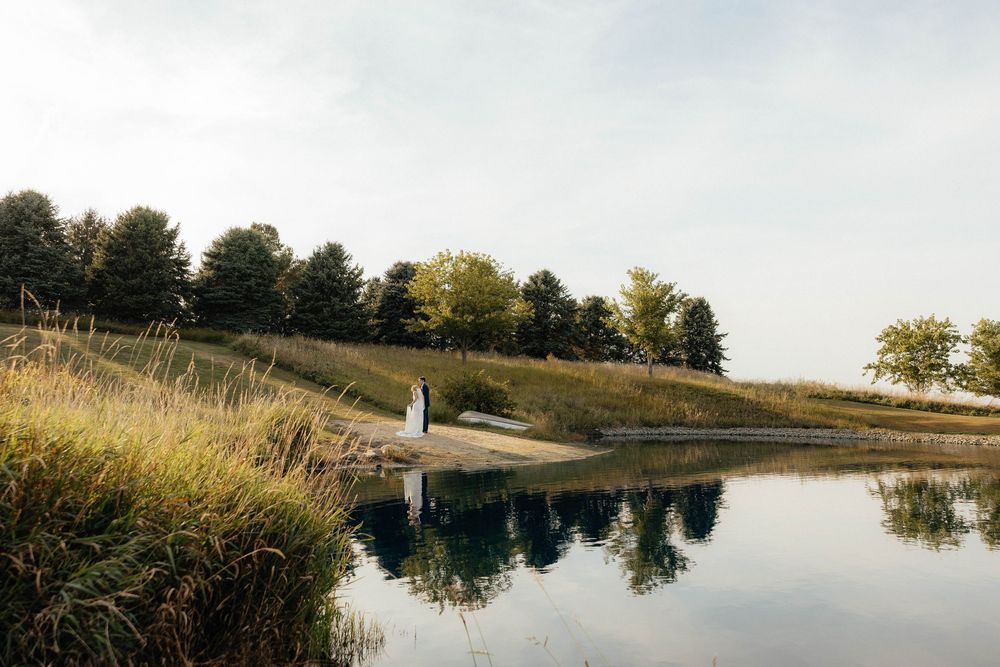 A serene pond reflects tall grass and trees along its banks on a tranquil autumn day.