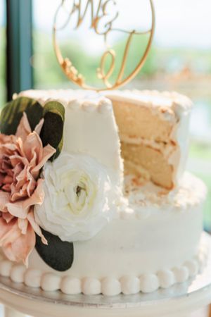Elegant white wedding cake decorated with pink and white flowers and a gold topper.
