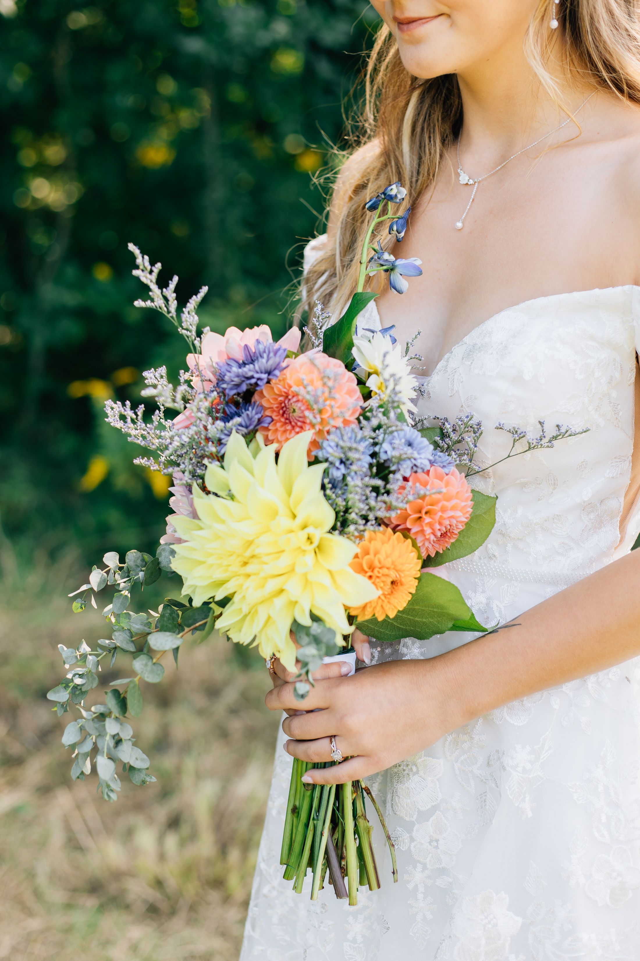 Close-up of a bridal bouquet with yellow dahlias, orange flowers, and purple accents against a white dress.