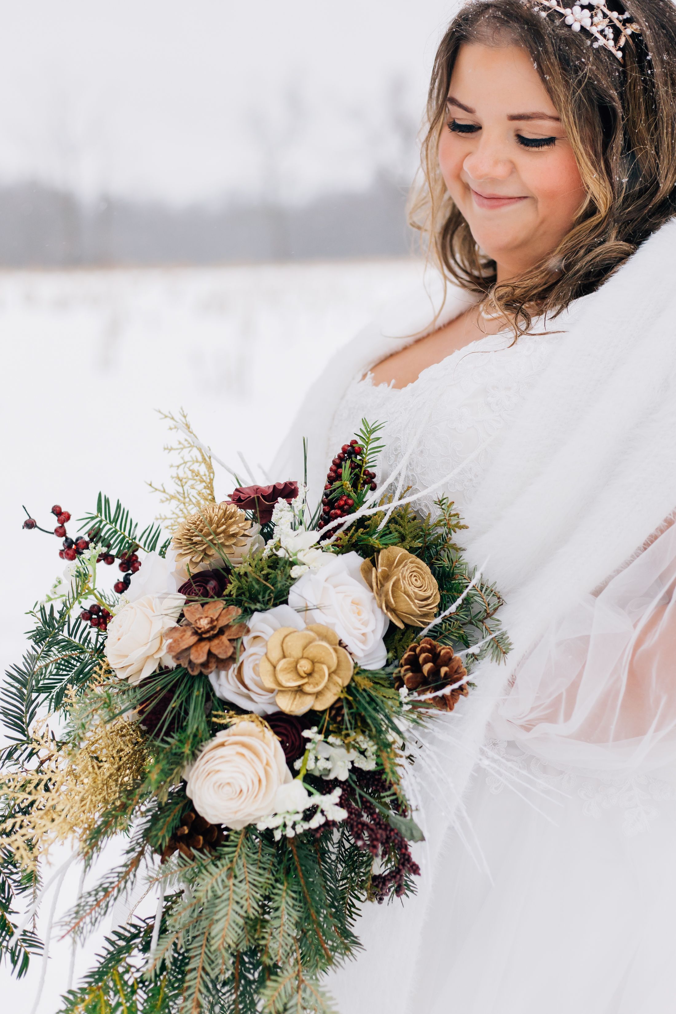 A winter bridal bouquet features white roses, evergreen sprigs, and burgundy accents.