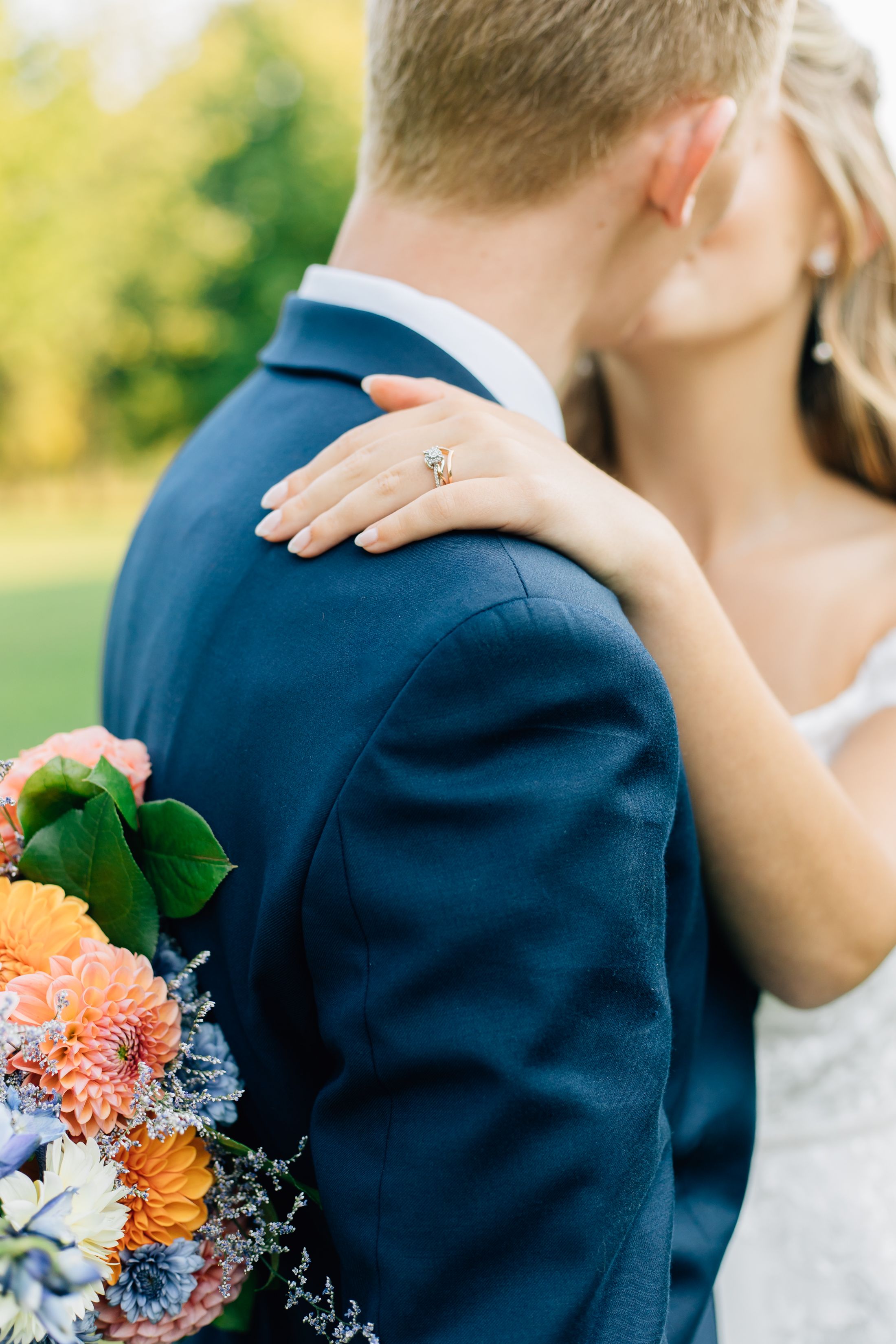 Close-up of a wedding couple embracing, showing engagement ring and bridal bouquet.
