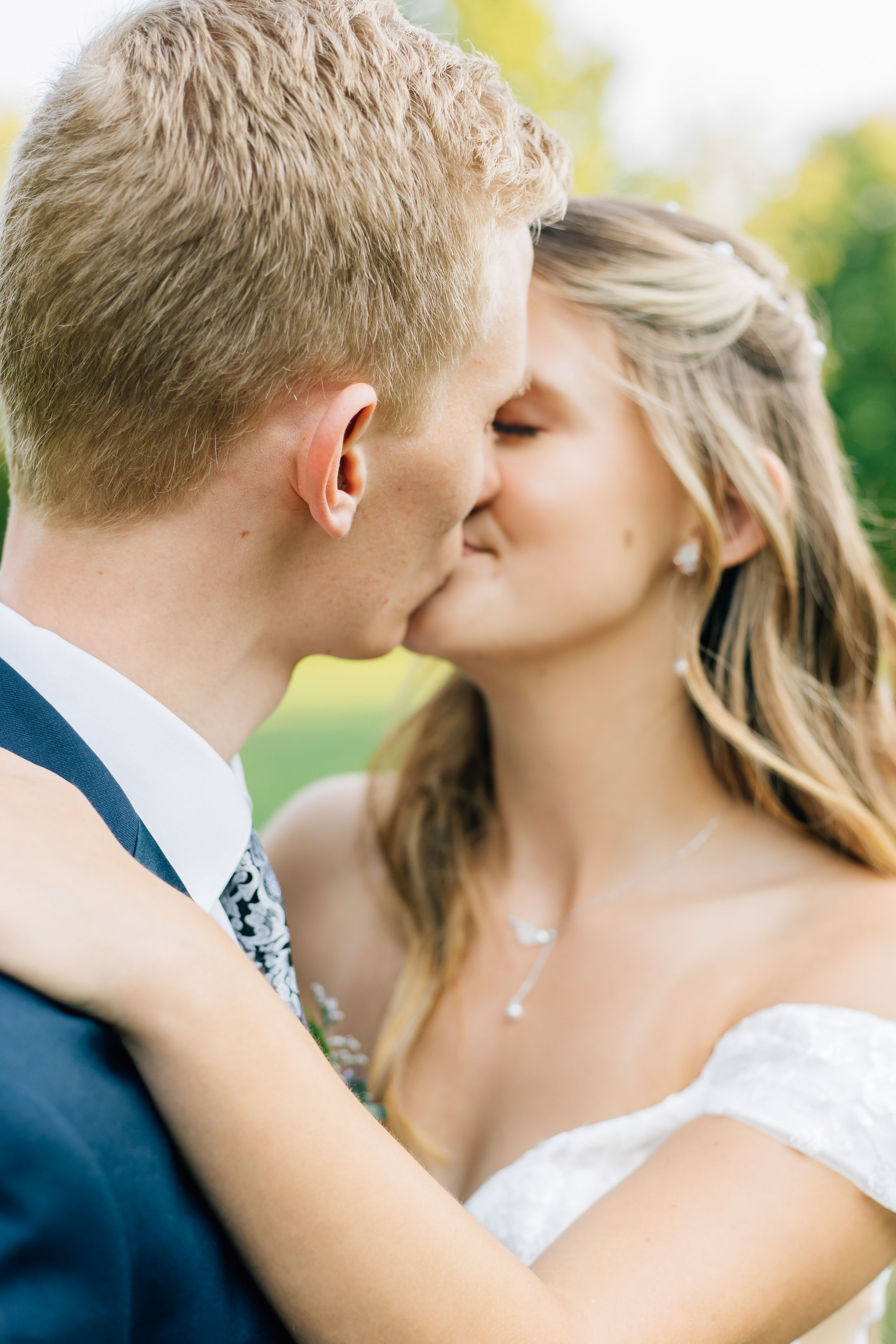 A romantic wedding kiss between newlyweds outdoors with soft natural lighting.