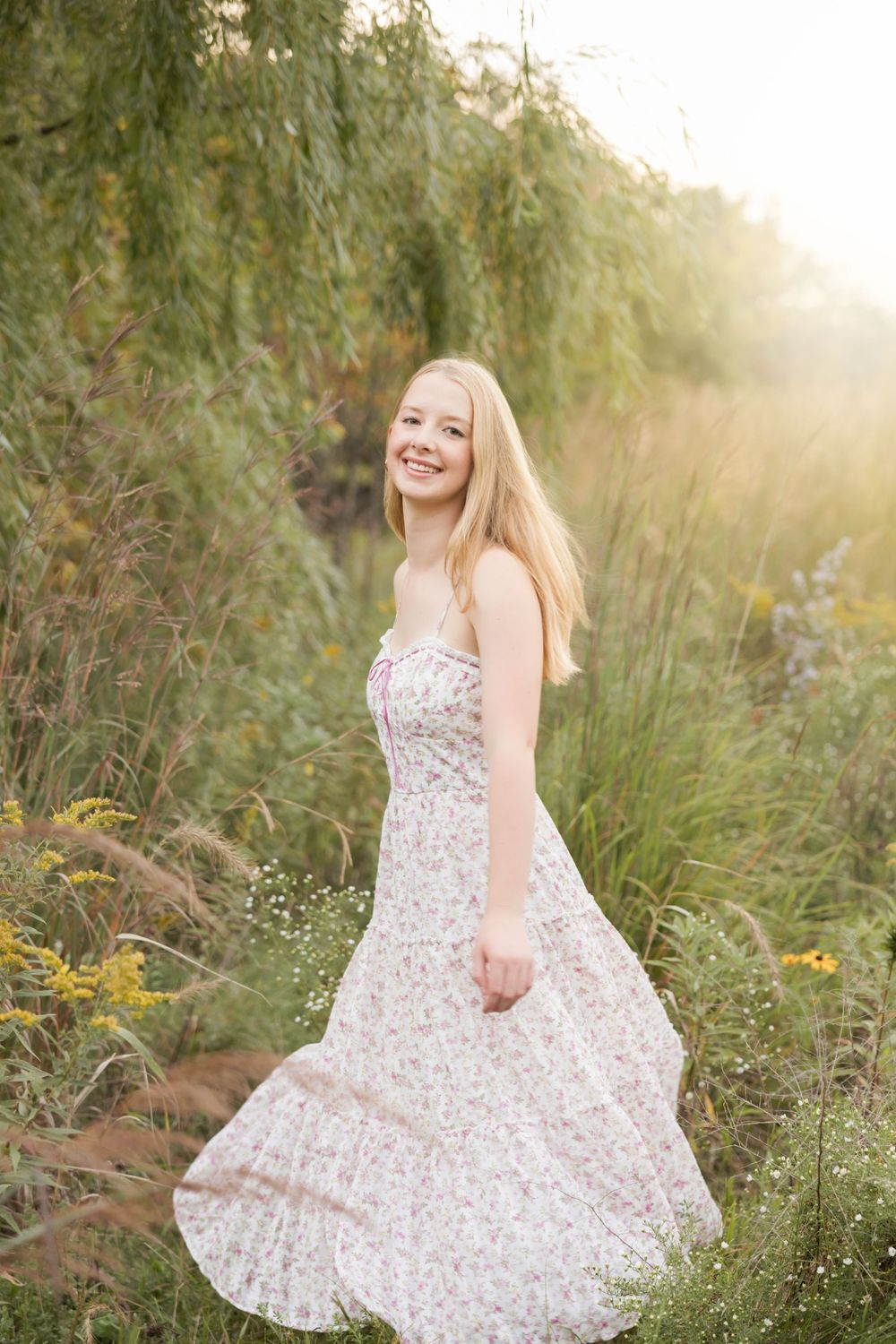A person in a floral sundress twirls joyfully in a sunlit meadow with tall grass and wildflowers.