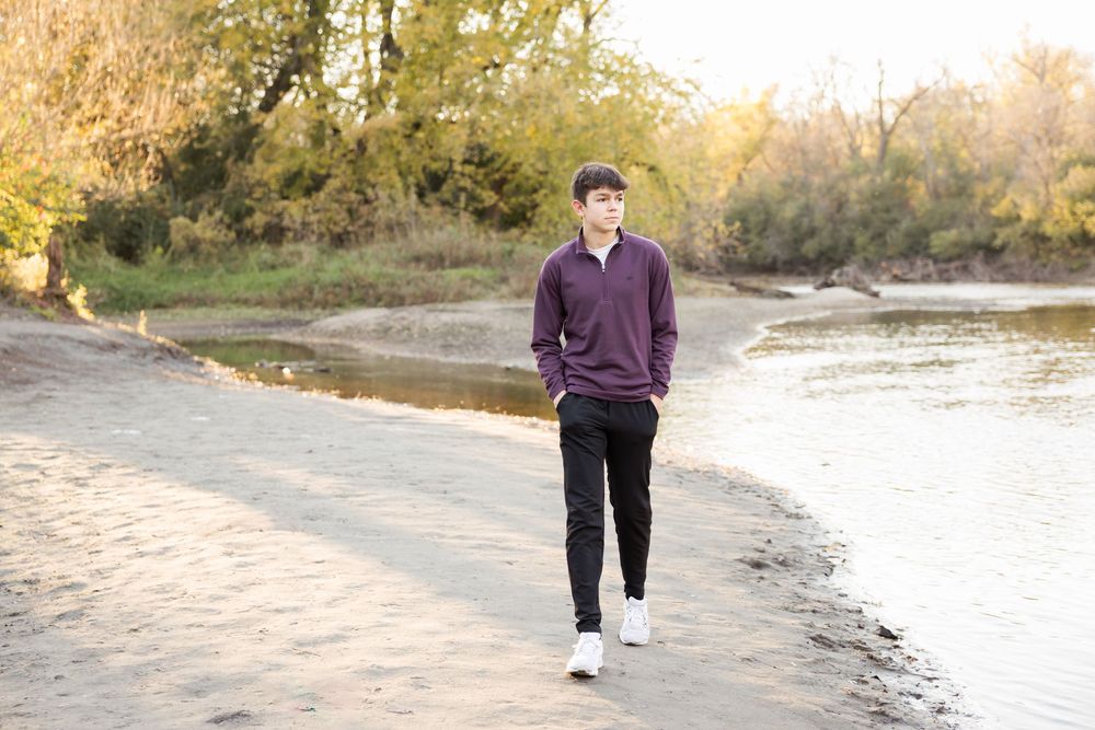 Person in purple sweater and dark pants walking along a scenic beach path during golden hour sunset.