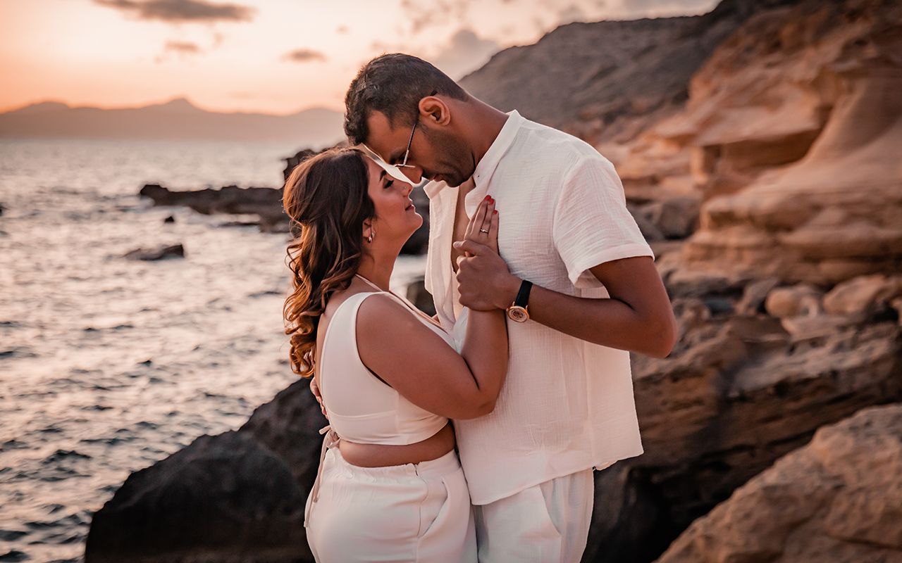 A honeymoon couple dressed all in white in a romantic pose, her hand on his heart during sunset.