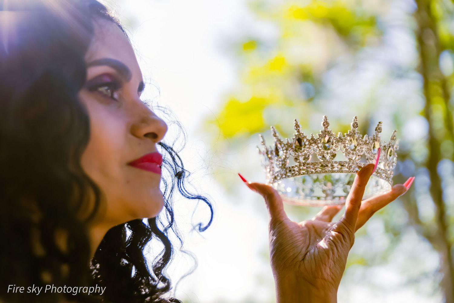 An artistic profile shot of someone holding a sparkling crown in sunlit natural setting.