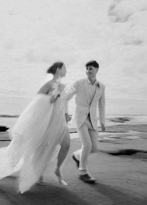 A couple in white attire runs playfully along a dark sandy beach in a romantic sequence of motion blur photographs.
