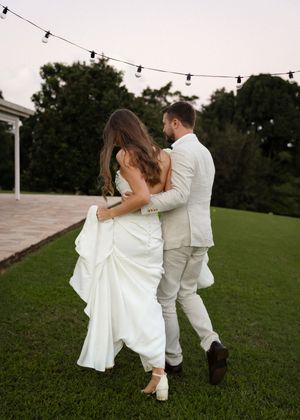 Couple walking together on grass under string lights at dusk.
