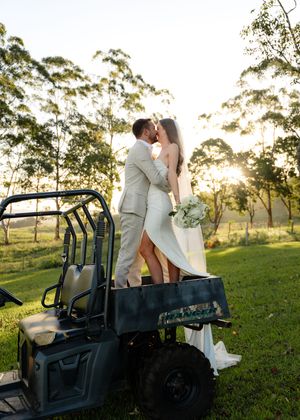 Newlyweds sharing a romantic moment on a utility vehicle in a scenic field.