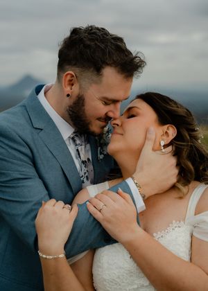 A romantic wedding couple share an intimate moment against a misty mountain backdrop.