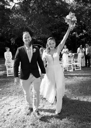 A joyful wedding celebration outdoors with a couple walking down the aisle as guests look on from white chairs.