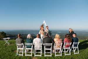 Intimate outdoor hilltop wedding ceremony with small group of guests seated in white chairs.