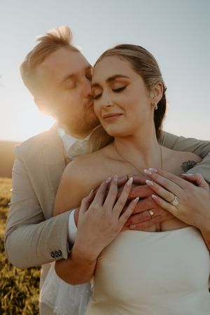 Tender wedding portrait at sunset with couple embracing and showing rings.