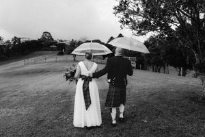 A couple poses together on a grassy hillside under umbrellas during their outdoor wedding photography session.