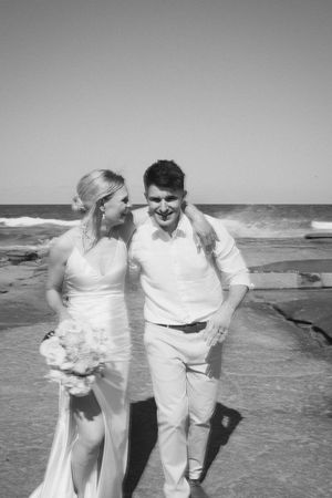 Couple in white outfits playing and laughing together on a beach.