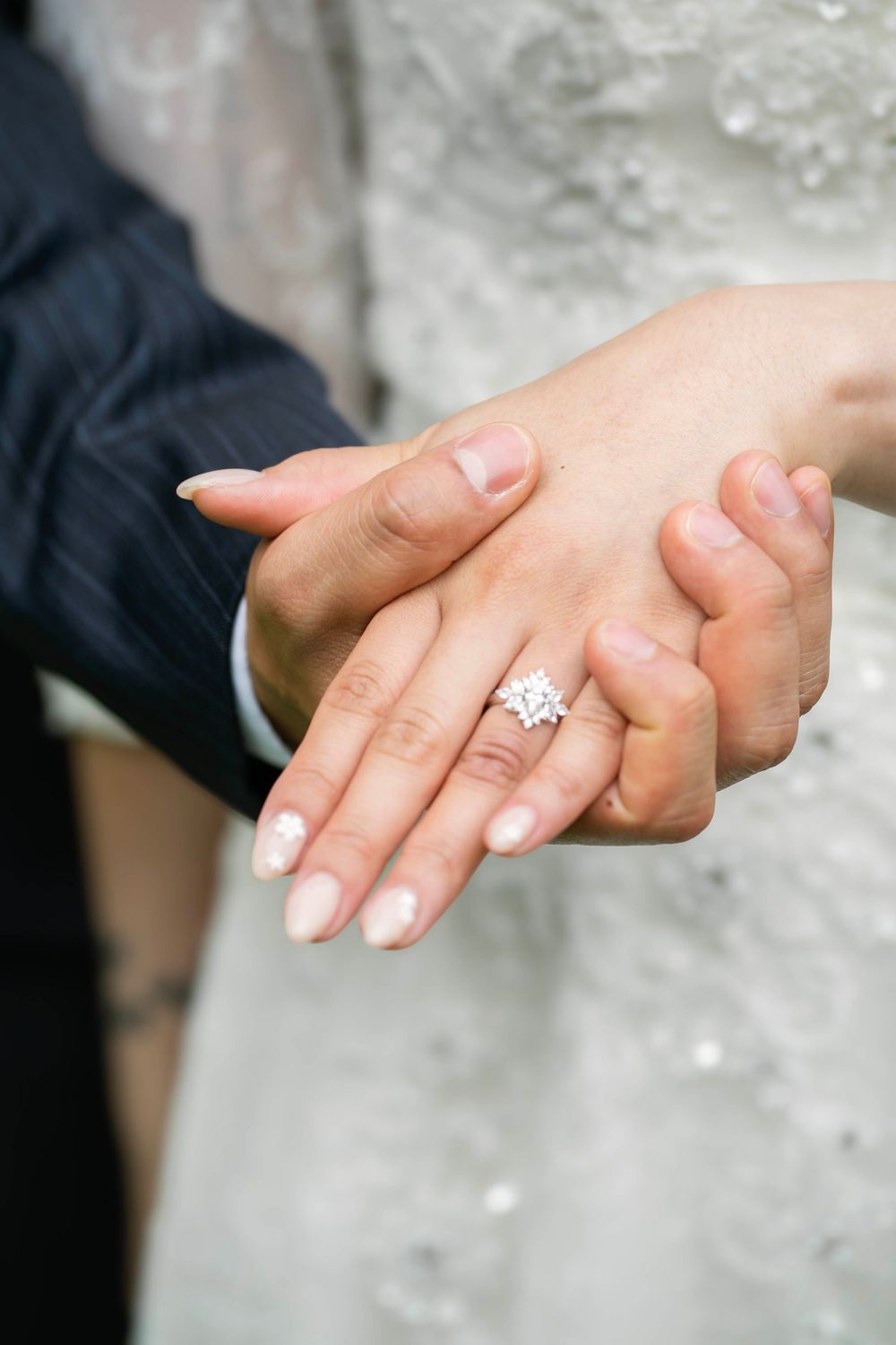 Close up of hands showing off an elegant diamond engagement ring with French manicured nails.
