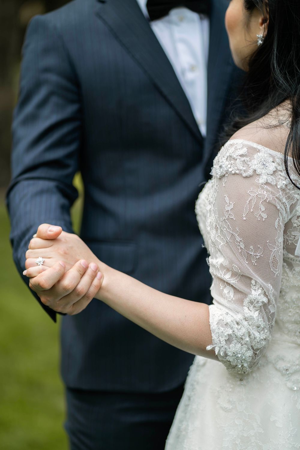 Close-up of bride and groom holding hands, showing lace sleeve detail of wedding dress and dark suit.