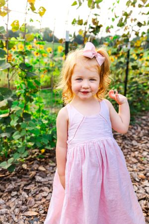 Little girl in pink dress poses in garden with sunflowers.
