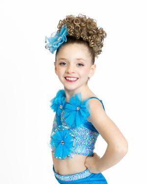 Young dancer in a sparkly blue performance costume with matching bow and curled updo.