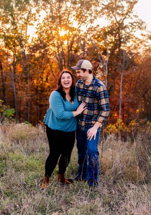 A couple shares a joyful moment at sunset in an autumn field with golden trees in the background.