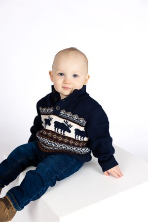 Baby in navy sweater with bear design sits against white background.