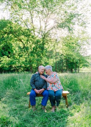 Elderly couple sharing tender moment while sitting on wooden bench in sunlit meadow.