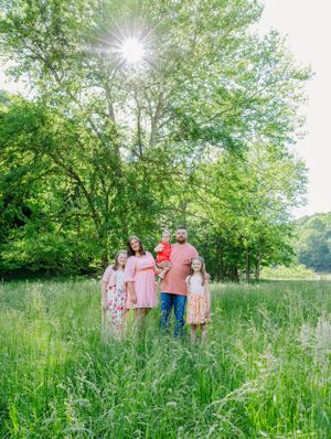 Family portrait in a sunlit meadow with tall grass and trees in the background.