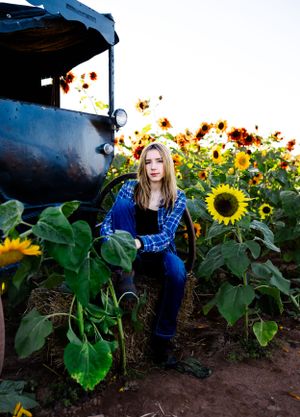 Portrait in sunflower field with vintage blue truck at sunset.