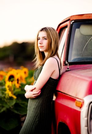 Green dress against red vintage truck with sunflower field backdrop during sunset photoshoot.