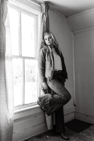 Black and white portrait by window in rustic room with natural lighting.