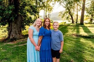 Mother and children in blue and light blue dresses pose together in sunlit garden setting.
