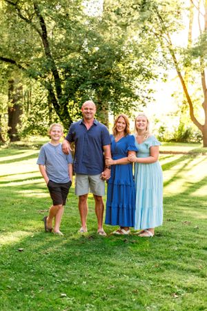 Happy family stands together on lush green lawn during golden hour photography session.