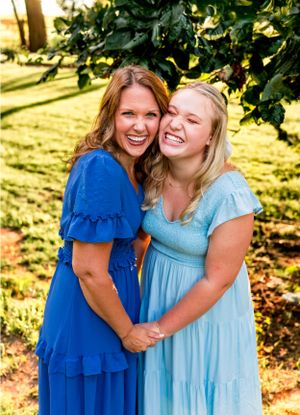 Two women in blue dresses share joyful moment together outdoors in warm sunlight.