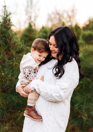 A sweet moment between parent and child in matching white sweaters among pine trees.