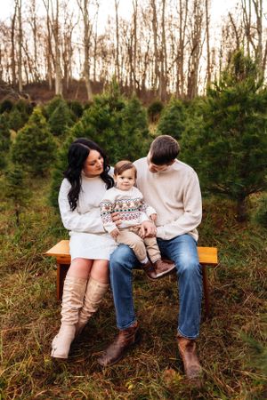 A family shares a tender moment while sitting on a wooden bench in a pine tree forest.