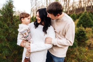 A family cuddles together in cozy sweaters among evergreen trees.