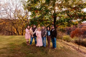 A group poses together on a hillside during autumn with colorful fall foliage in the background.