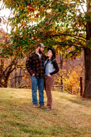A couple shares an intimate moment under fall trees with golden sunlight filtering through.