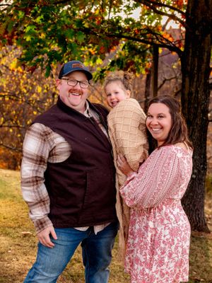 A family shares a warm embrace while standing beneath autumn trees in a park setting.