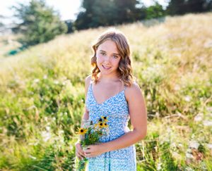 Woman in blue sundress holds sunflowers while standing in golden summer field.