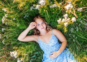 Young woman in blue dress lies in flowering meadow during summer photoshoot.