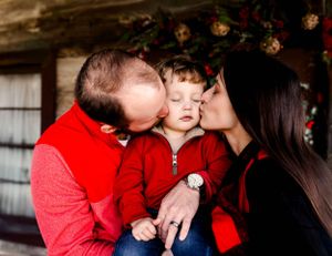 Family wearing red shares intimate moment against rustic backdrop with holiday decorations.