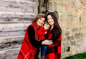 Family in matching buffalo plaid outfits poses against weathered wall.