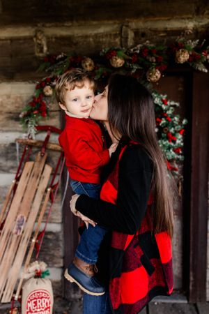 Tender moment captured on rustic porch with holiday decorations and vintage sled.