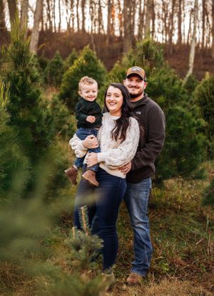 Group poses casually together among evergreen trees at Christmas tree farm.